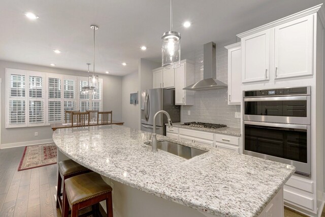 kitchen featuring a large island, wall chimney range hood, and sink