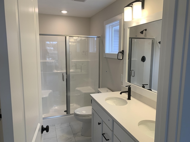 bathroom featuring double vanity, a stall shower, toilet, marble finish floor, and a sink