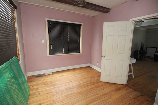 unfurnished bedroom featuring beam ceiling and light hardwood / wood-style flooring