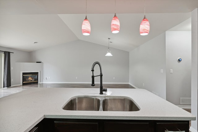 kitchen featuring light stone countertops, decorative light fixtures, vaulted ceiling, and sink