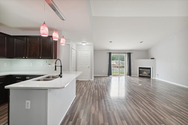 kitchen with a center island with sink, sink, hanging light fixtures, tasteful backsplash, and dark brown cabinets