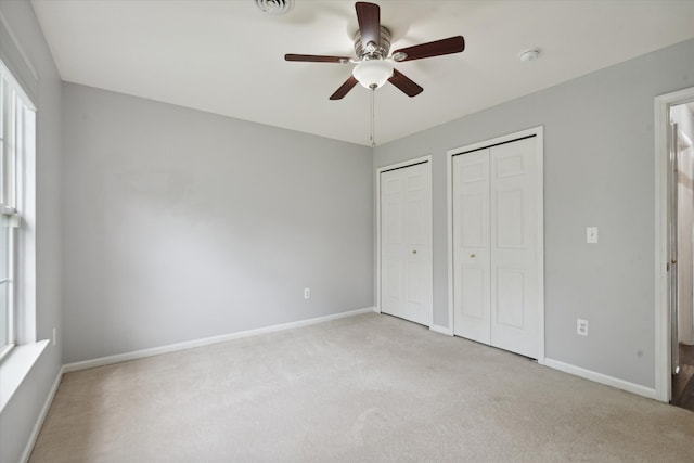 unfurnished bedroom featuring two closets, light colored carpet, and ceiling fan