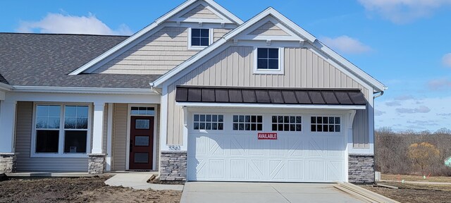 view of front facade featuring roof with shingles, an attached garage, a standing seam roof, stone siding, and driveway