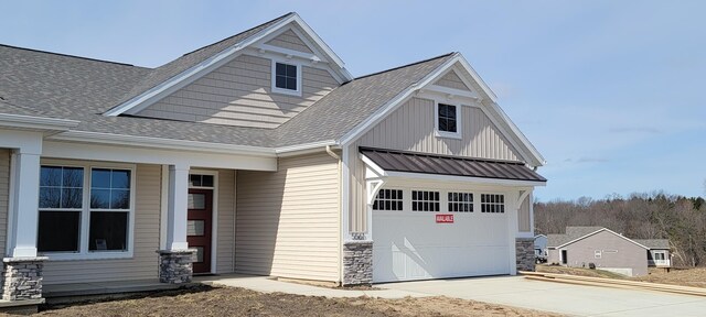 view of front of property with driveway, a shingled roof, stone siding, an attached garage, and board and batten siding