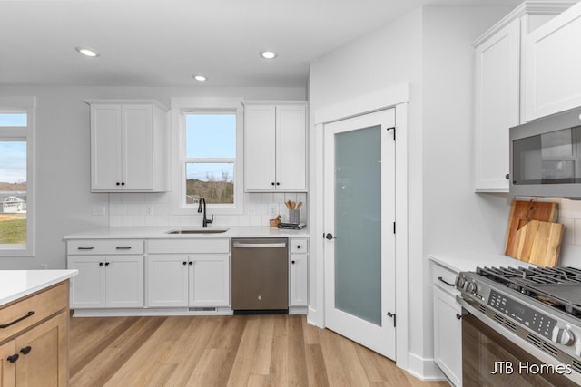 kitchen featuring decorative backsplash, appliances with stainless steel finishes, light wood-type flooring, a sink, and light countertops