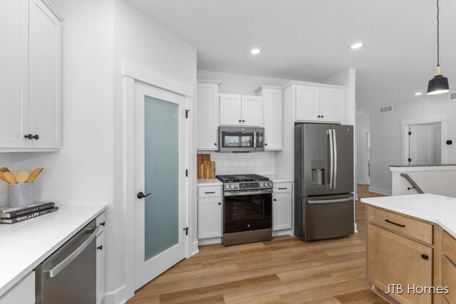kitchen featuring appliances with stainless steel finishes, light countertops, light wood-style flooring, decorative backsplash, and visible vents