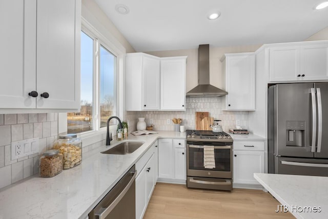 kitchen featuring a sink, stainless steel appliances, white cabinets, wall chimney range hood, and light stone countertops