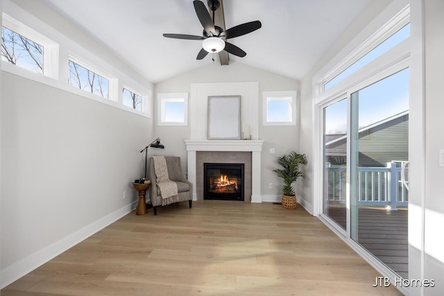 sitting room featuring a ceiling fan, baseboards, light wood-style flooring, vaulted ceiling, and a glass covered fireplace