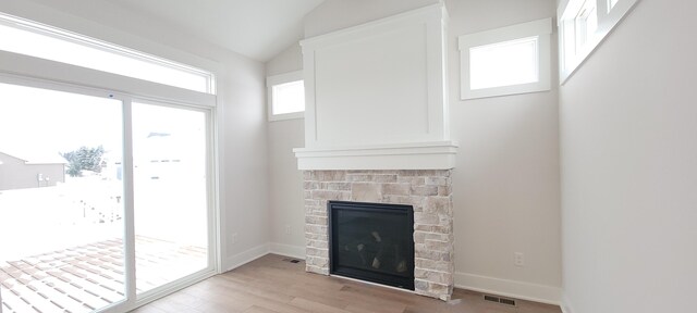 unfurnished living room featuring baseboards, visible vents, a stone fireplace, vaulted ceiling, and light wood-type flooring