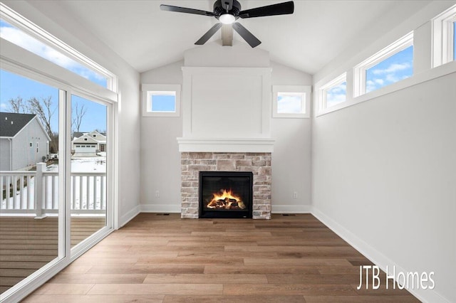 unfurnished living room with light wood-style flooring, a warm lit fireplace, baseboards, and a ceiling fan