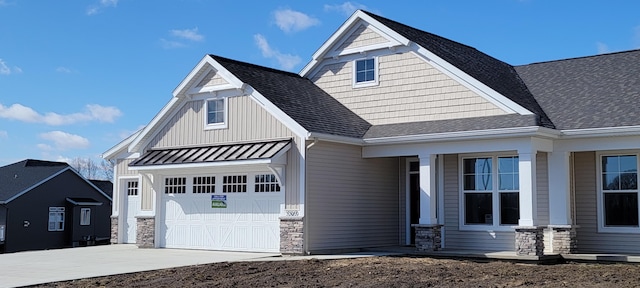 craftsman inspired home with board and batten siding, roof with shingles, a garage, stone siding, and driveway