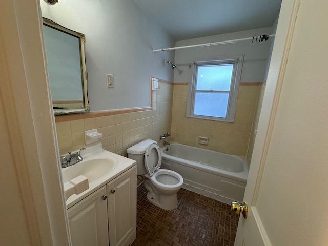 full bathroom featuring tiled shower / bath, vanity, toilet, and tile walls