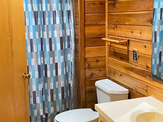 bathroom with toilet, vanity, and wood walls