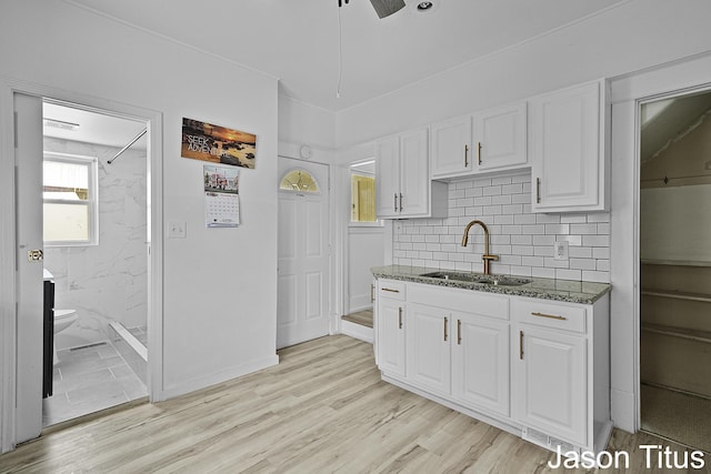 kitchen featuring sink, dark stone countertops, decorative backsplash, white cabinets, and light wood-type flooring