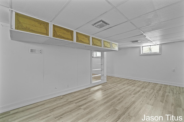 basement with light wood-type flooring and a paneled ceiling