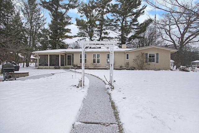 snow covered back of property with a pergola and a sunroom