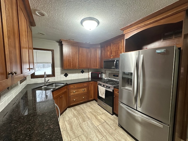 kitchen featuring sink, backsplash, dark stone countertops, a textured ceiling, and appliances with stainless steel finishes