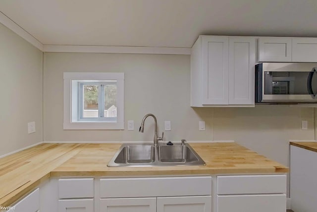 kitchen featuring white cabinets, wooden counters, crown molding, and sink