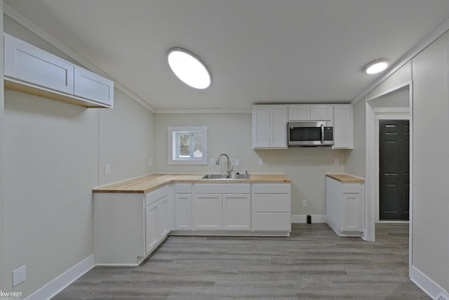 kitchen featuring crown molding, sink, light hardwood / wood-style flooring, butcher block countertops, and white cabinetry