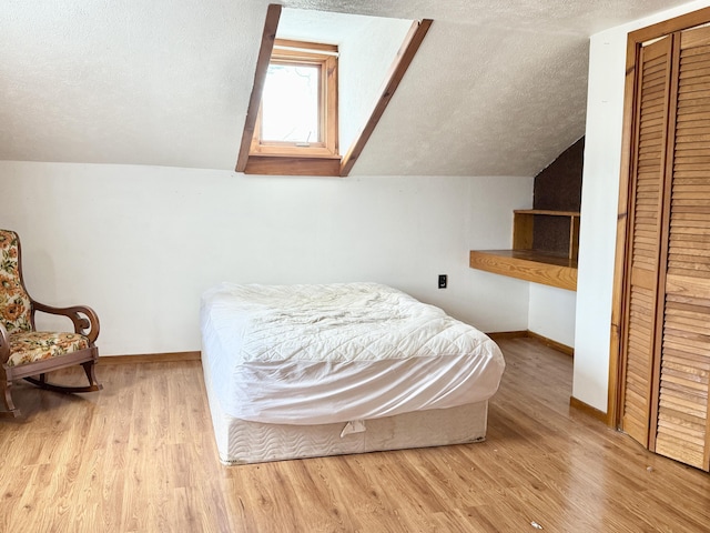 bedroom with a textured ceiling, light hardwood / wood-style floors, a closet, and lofted ceiling