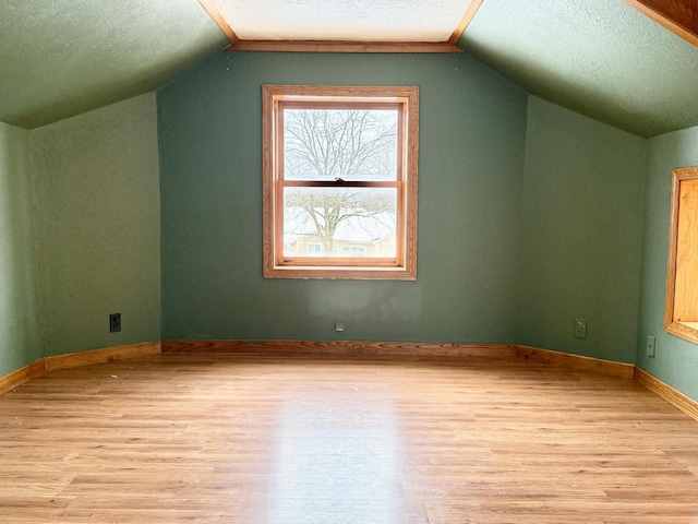 additional living space featuring a textured ceiling, light hardwood / wood-style flooring, and lofted ceiling