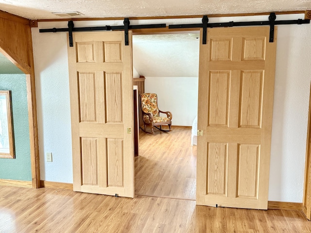 corridor featuring a barn door, wood-type flooring, and a textured ceiling