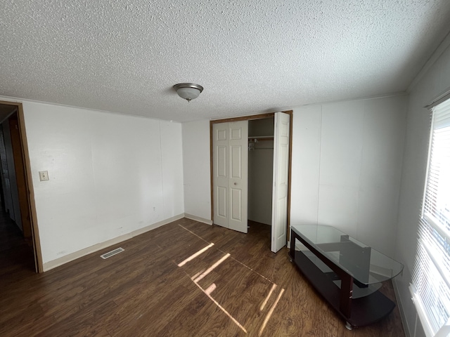 unfurnished bedroom with a textured ceiling, a closet, and dark wood-type flooring