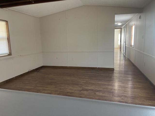 spare room with a textured ceiling, dark wood-type flooring, and vaulted ceiling