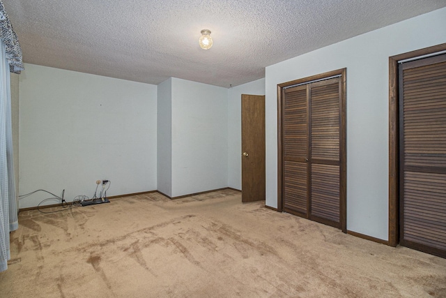 unfurnished bedroom with a textured ceiling, light carpet, and multiple closets