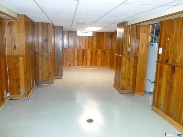 basement featuring a drop ceiling, wood walls, and water heater