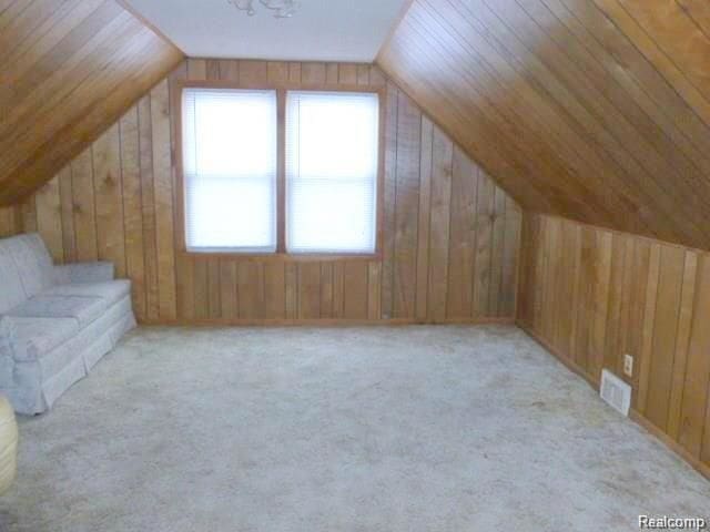 additional living space with wood walls, light colored carpet, and lofted ceiling