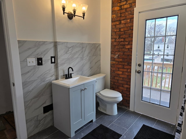 bathroom featuring an inviting chandelier, tile patterned flooring, toilet, vanity, and tile walls