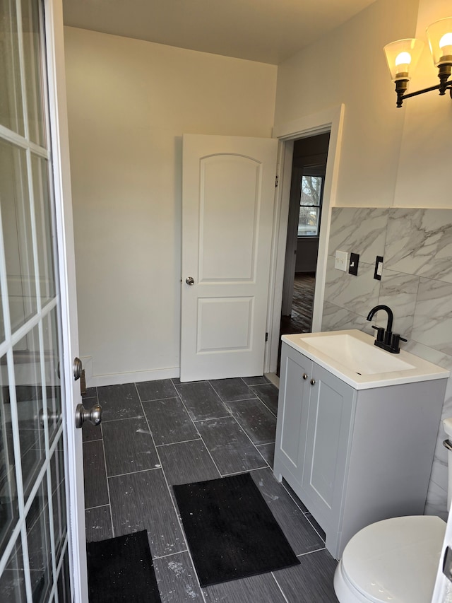 bathroom featuring vanity, toilet, tile walls, and a chandelier