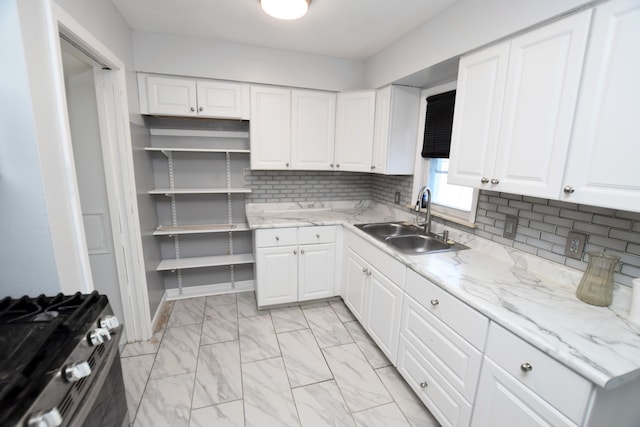 kitchen featuring light stone countertops, stainless steel gas range, white cabinetry, sink, and backsplash