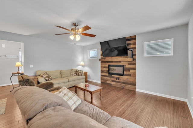 living room featuring ceiling fan, a large fireplace, and light hardwood / wood-style flooring