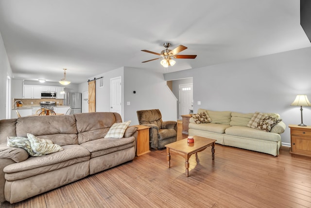 living room with ceiling fan, a barn door, and light hardwood / wood-style floors