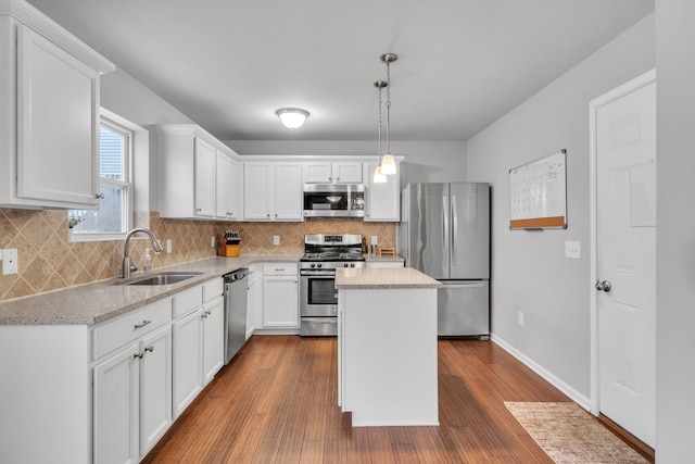 kitchen with stainless steel appliances, sink, pendant lighting, white cabinets, and a center island