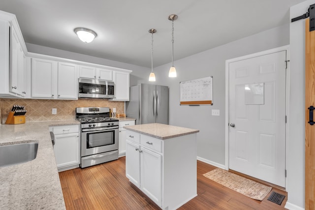 kitchen featuring hanging light fixtures, decorative backsplash, a kitchen island, white cabinetry, and stainless steel appliances