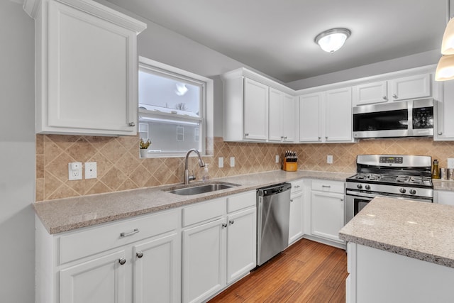 kitchen featuring decorative backsplash, stainless steel appliances, sink, white cabinetry, and hanging light fixtures