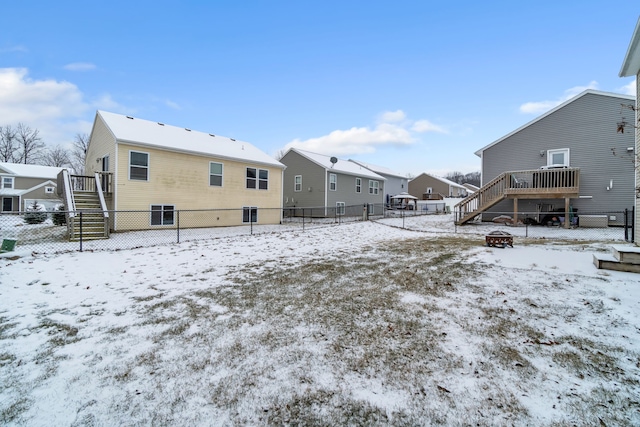 snow covered back of property with a deck and an outdoor fire pit