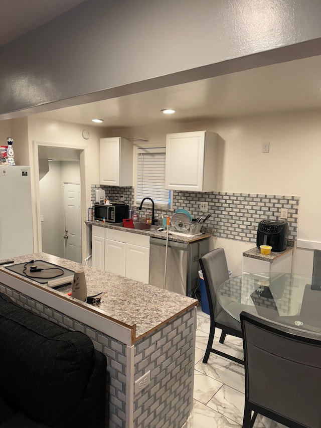 kitchen with white refrigerator, sink, stainless steel dishwasher, decorative backsplash, and white cabinetry