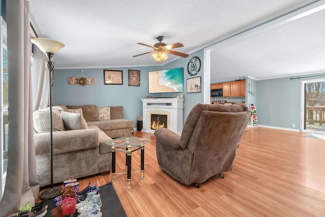 living room with a textured ceiling, ceiling fan, light wood-type flooring, and crown molding