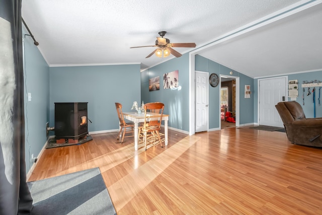 interior space featuring a wood stove, vaulted ceiling, ceiling fan, ornamental molding, and wood-type flooring