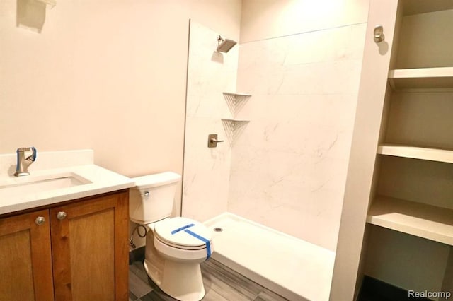 bathroom featuring toilet, wood-type flooring, vanity, and tiled shower