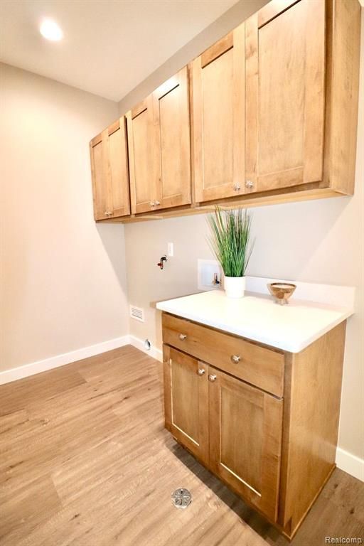 laundry area featuring washer hookup, light wood-type flooring, and cabinets