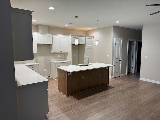 kitchen with sink, white cabinets, hardwood / wood-style flooring, an island with sink, and hanging light fixtures