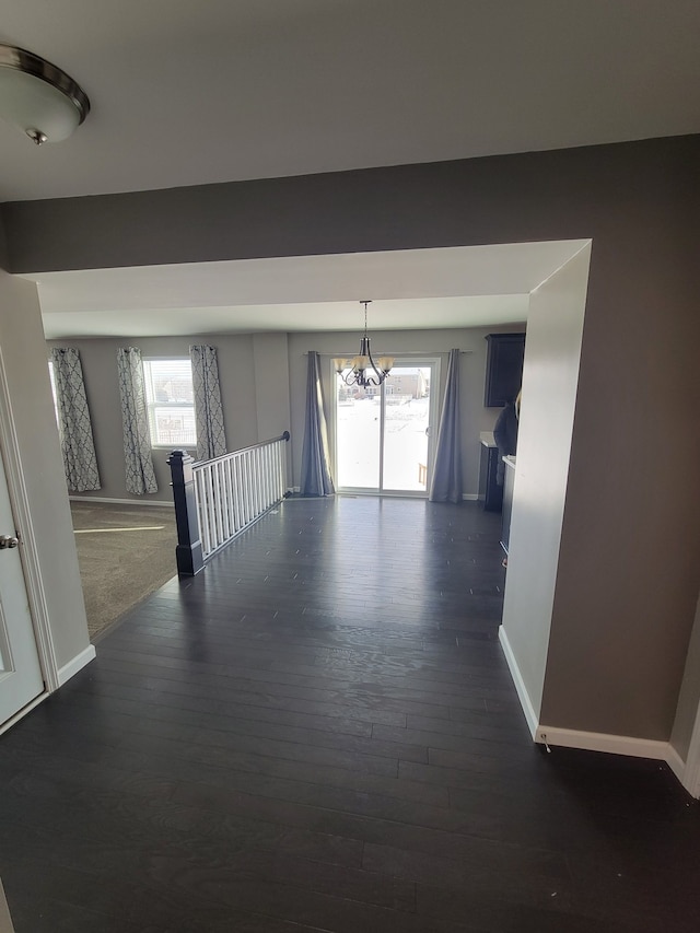 corridor with a healthy amount of sunlight, dark hardwood / wood-style flooring, and a notable chandelier