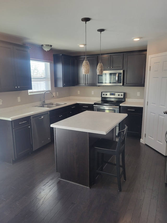 kitchen with dark hardwood / wood-style floors, hanging light fixtures, stainless steel appliances, a kitchen island, and sink