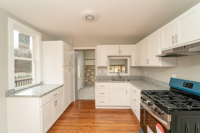 kitchen with stainless steel gas range oven, sink, white cabinets, and light hardwood / wood-style floors