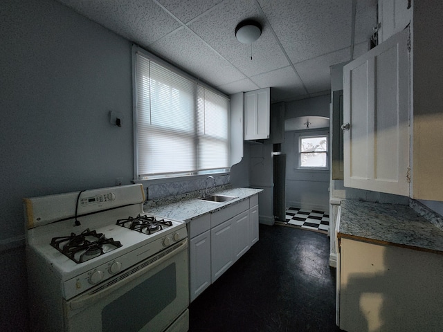 kitchen featuring white cabinets, white gas range oven, a drop ceiling, and sink